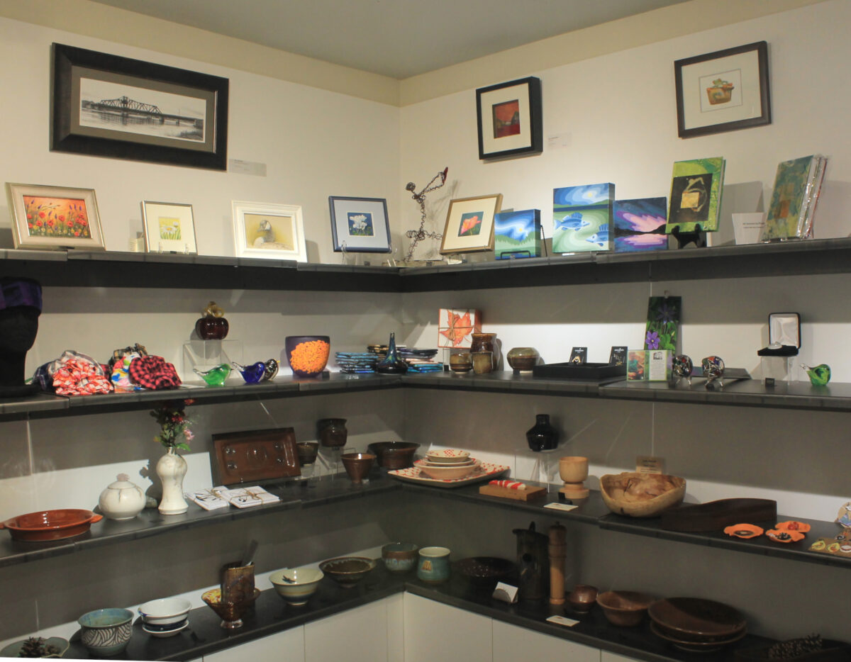 three shelves in the art gallery gift shop with paintings, stoneware and glass birds