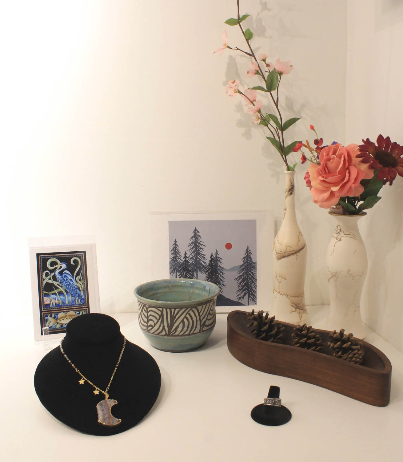 Moon shaped necklace on a black display beside a silver ring, cards, a green ceramic bowl