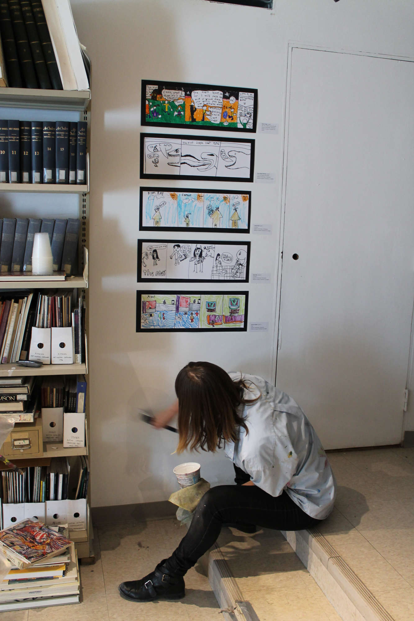 a volunteer is seated on a step and doing touch up painting on a wall in the library